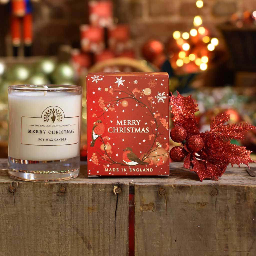 Christmas candle and packaging on a wooden surface with festive decorations in the background