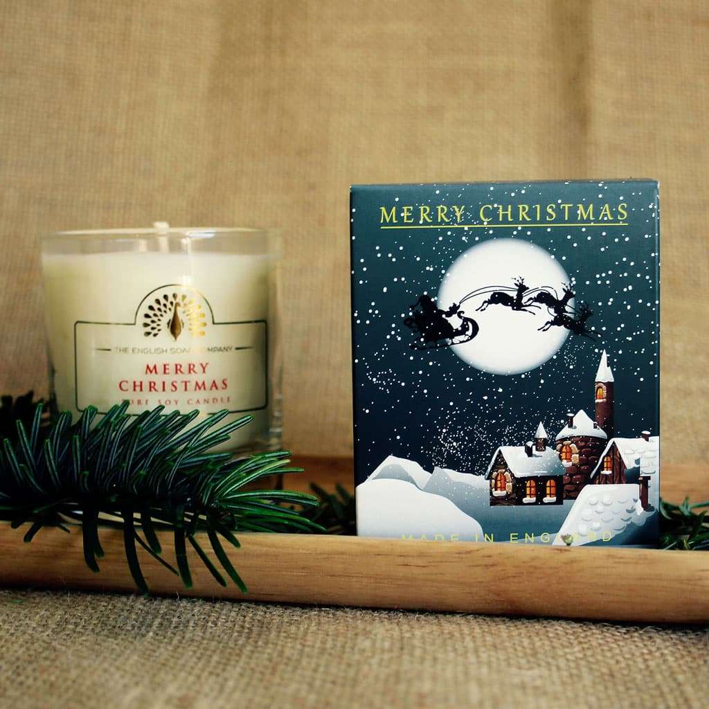 Merry Christmas soy candle in glass jar with matching box featuring a winter village scene and Santa's sleigh.