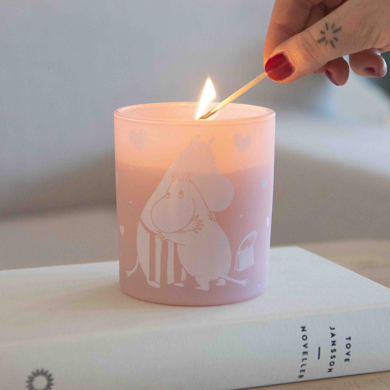 Pink candle with a dog design being lit on a book