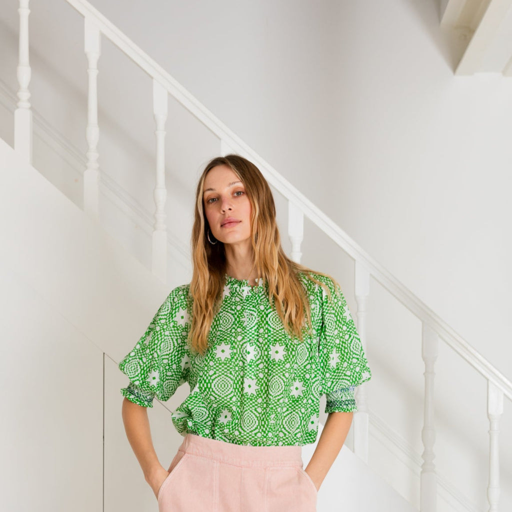 Woman wearing a Bonte patterned blouse in pink, navy, and cream, standing in front of a staircase.