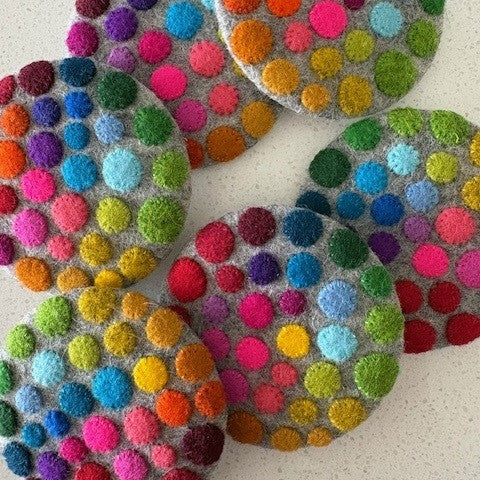 Colorful round coasters with multicolored pom-poms on a light background