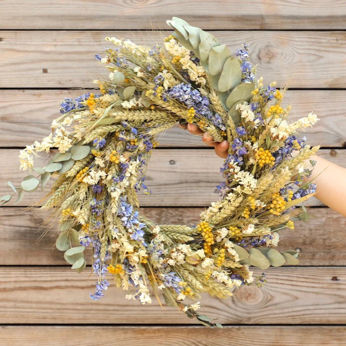 Dried flower wreath in shades of yellow, cream, and blue, incorporating wheat and eucalyptus.