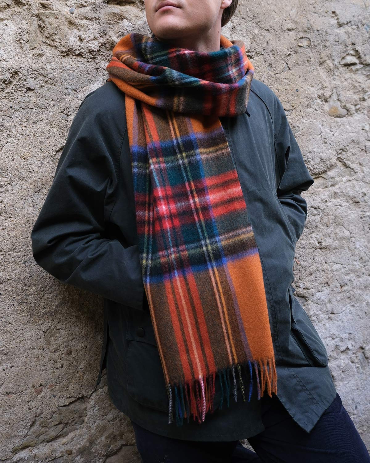 Person wearing a plaid scarf against a stone wall