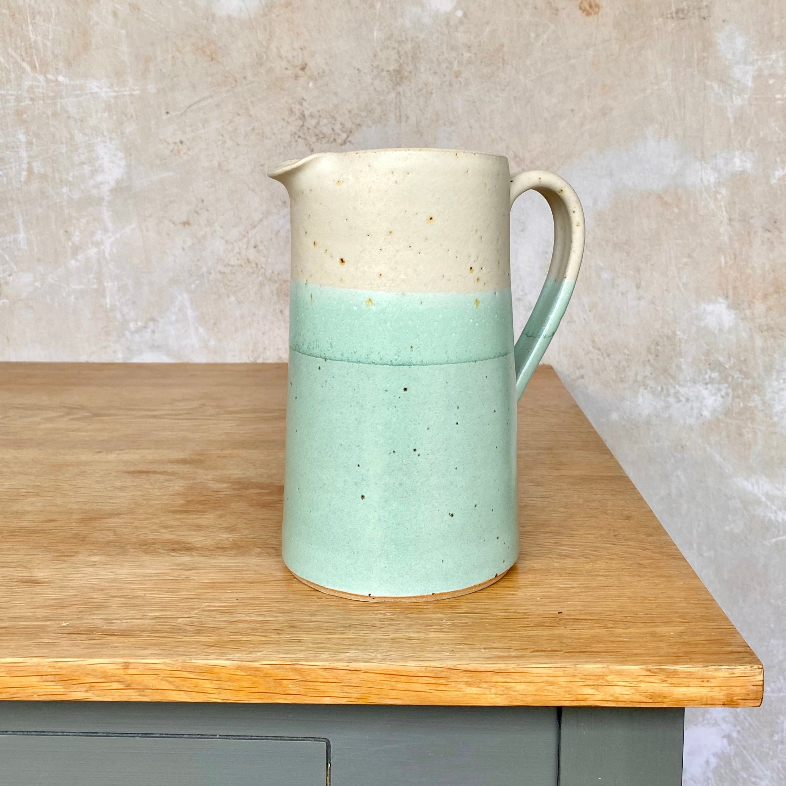 Cream and light teal speckled ceramic pitcher with a handle.