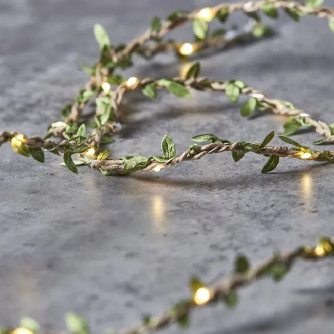 Warm-white LED string lights woven with jute twine and adorned with small green fabric leaves.