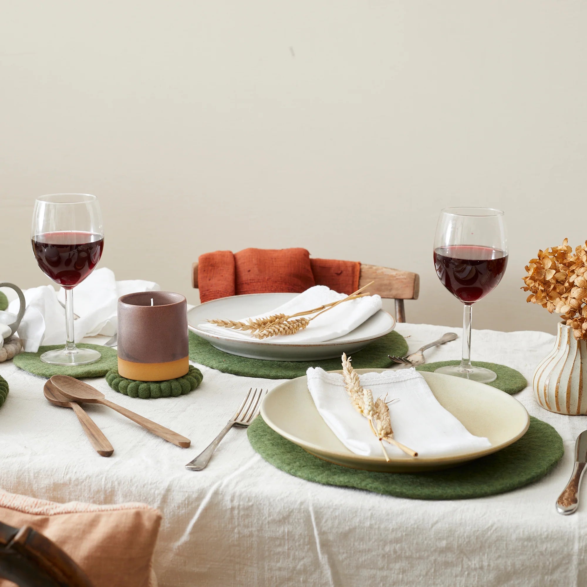 Two place settings with green felt coasters, ceramic plates, and white napkins adorned with wheat stalks.