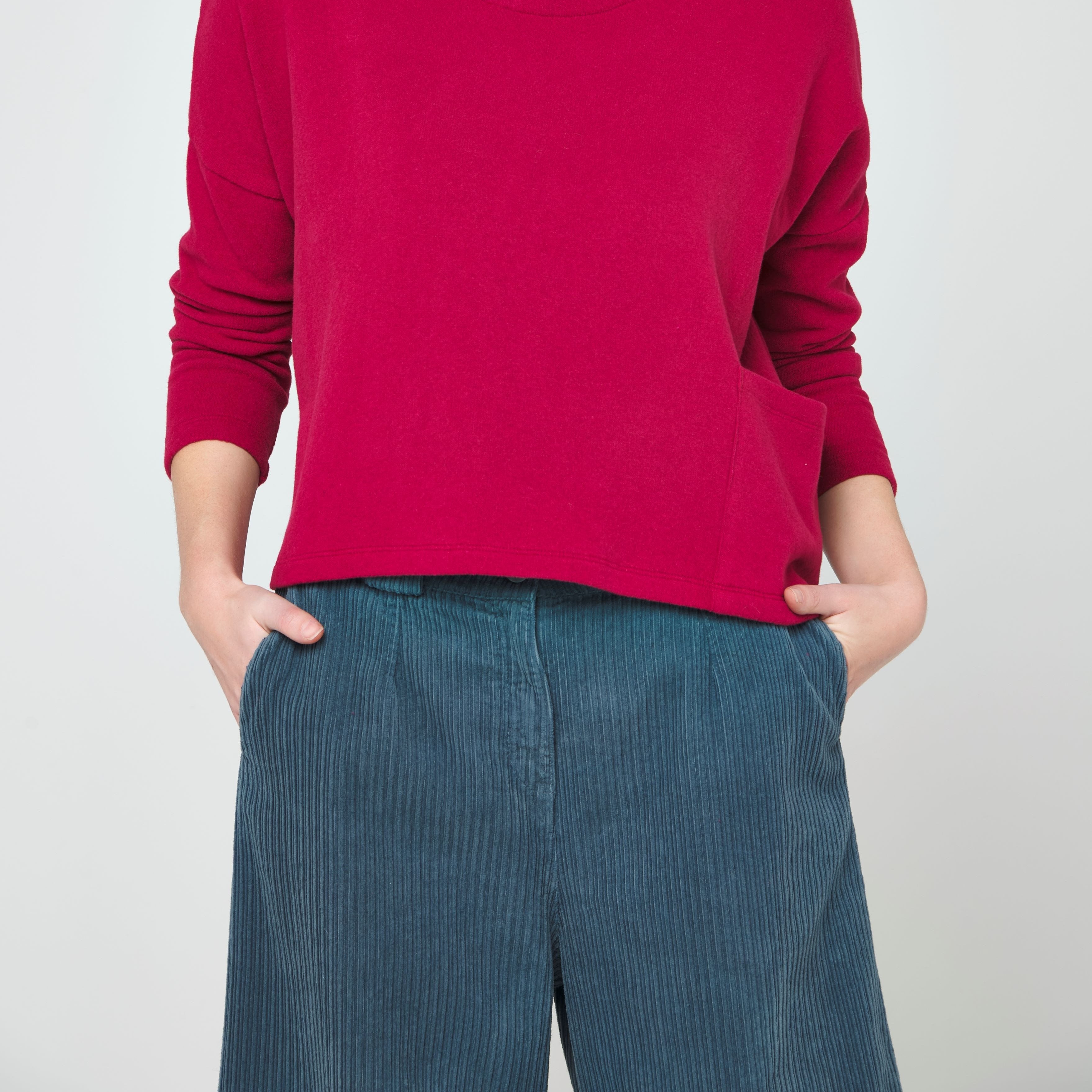 Crimson cropped sweater and teal corduroy pants.  The pants have a wide leg and visible vertical corduroy texture.