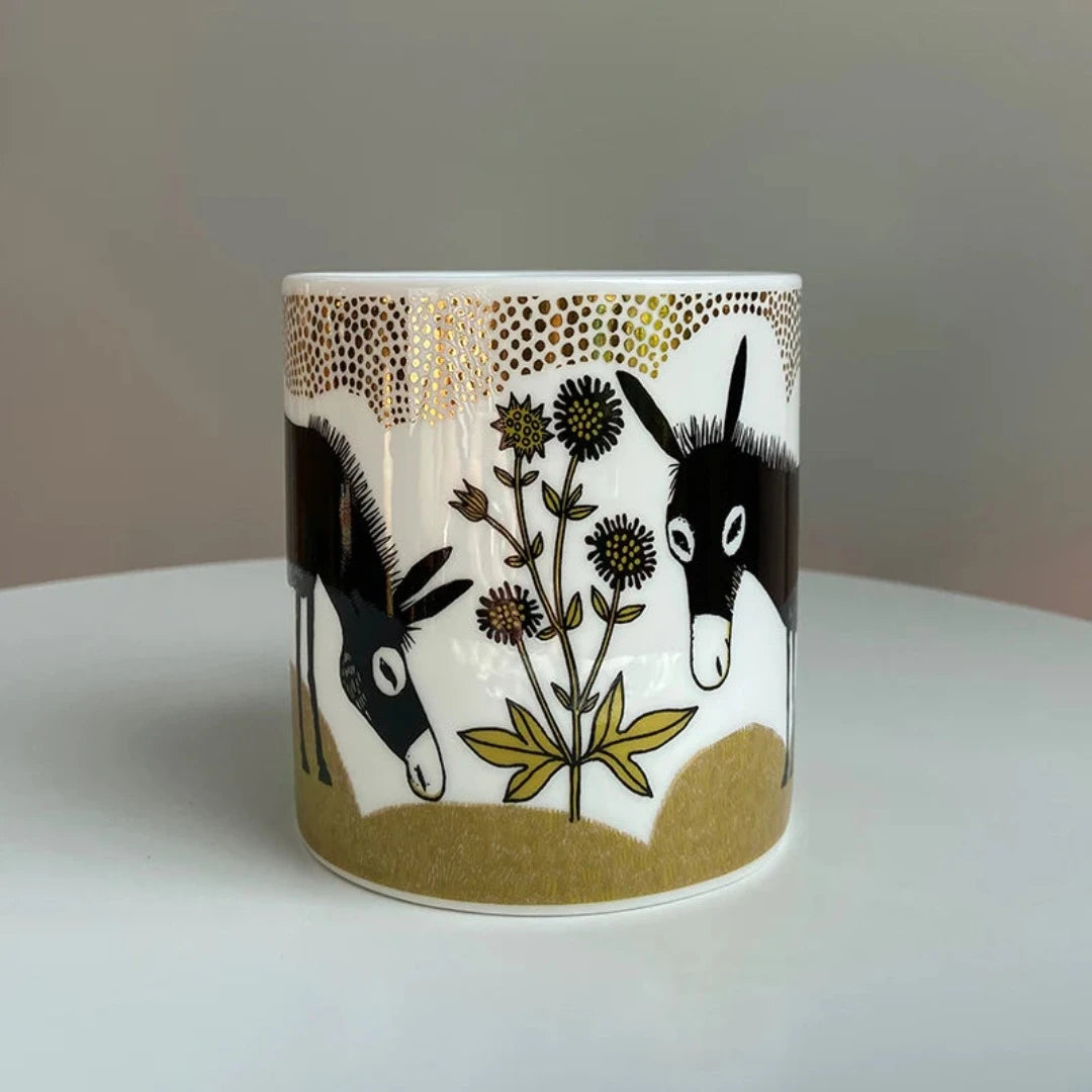 Cylindrical mug featuring two black donkeys and gold floral design.  Gold detailing accents the rim.
