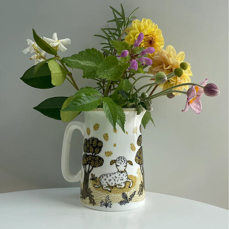 White ceramic pitcher with a lamb and stylized trees design in gold and black.