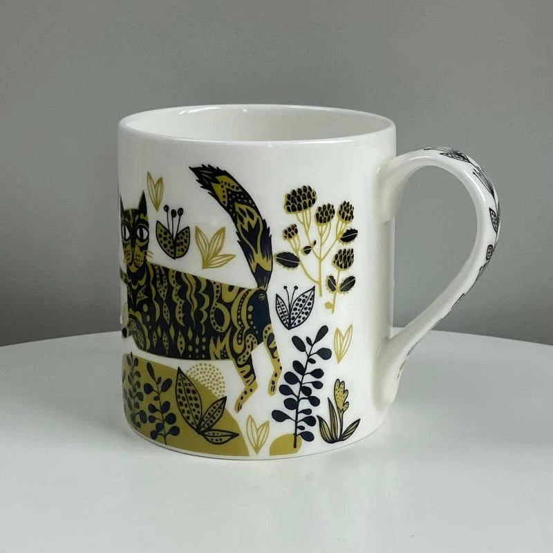 White mug with black and gold cat and floral pattern on a gray background
