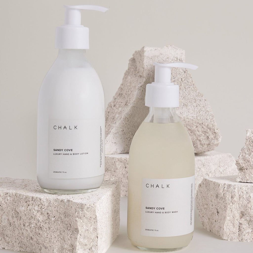 Two Chalk UK bottles of hand wash and lotion; one is white, the other is light beige, placed on textured stones.