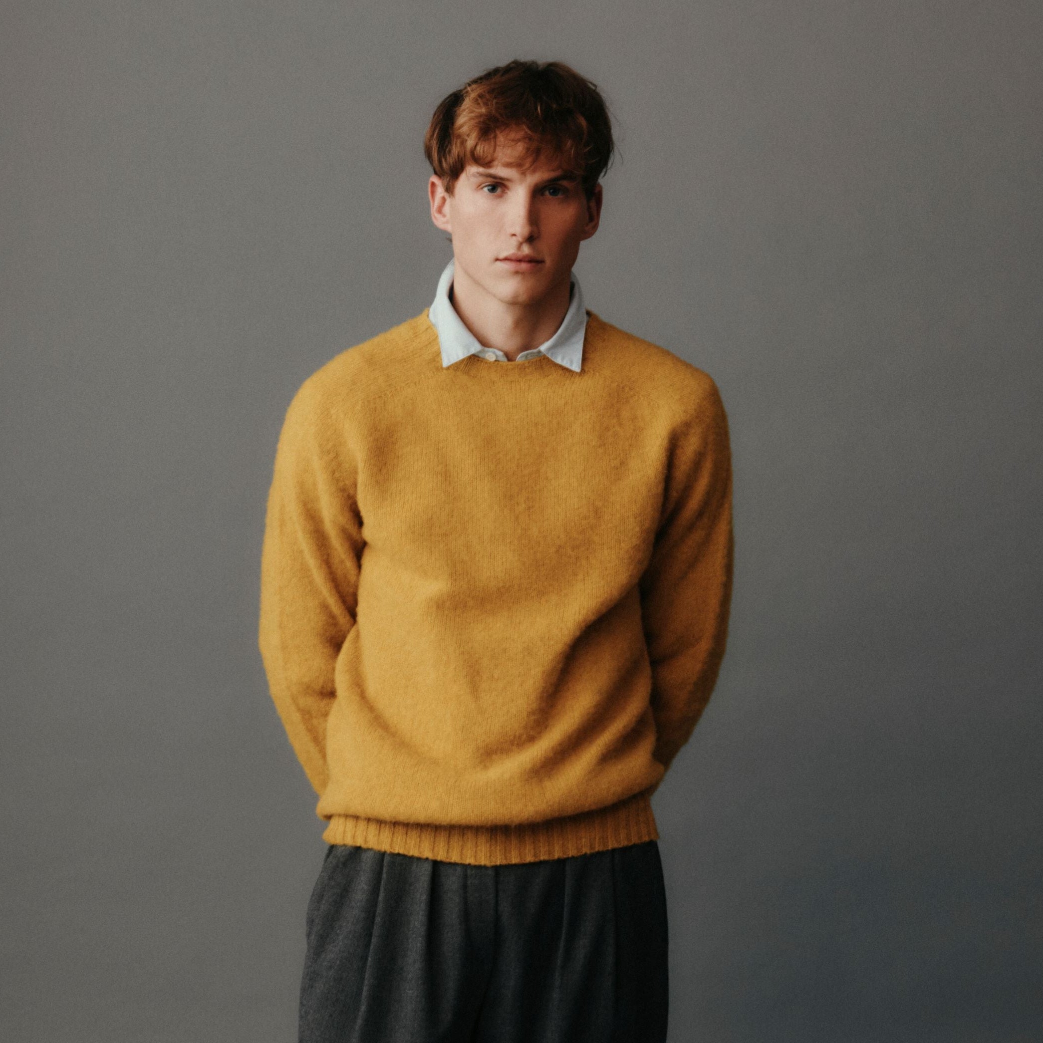 Man wearing a mustard yellow sweater over a white shirt on a gray background