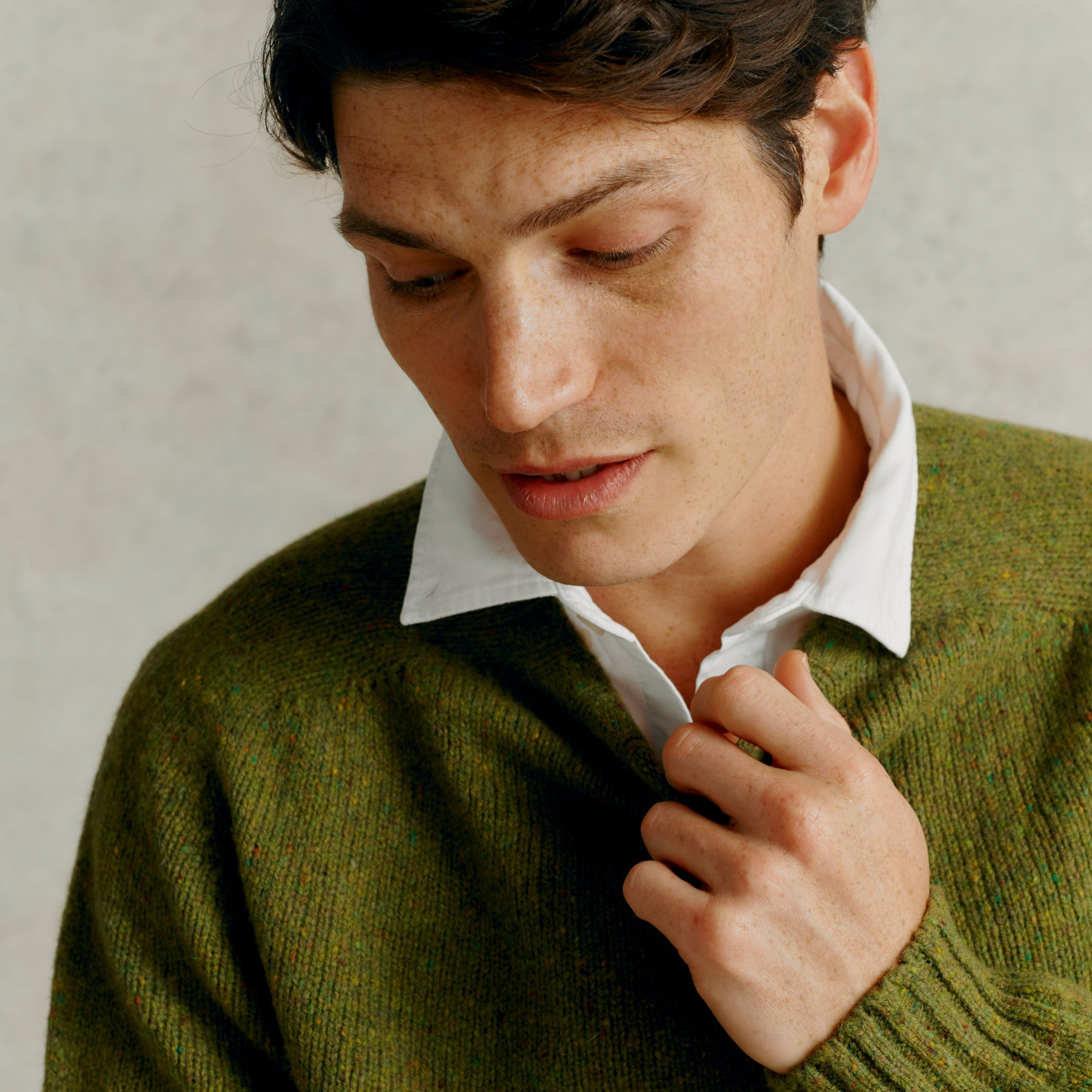 Close-up of a man's olive green, speckled knit cardigan. The cardigan is textured and features a relaxed fit.