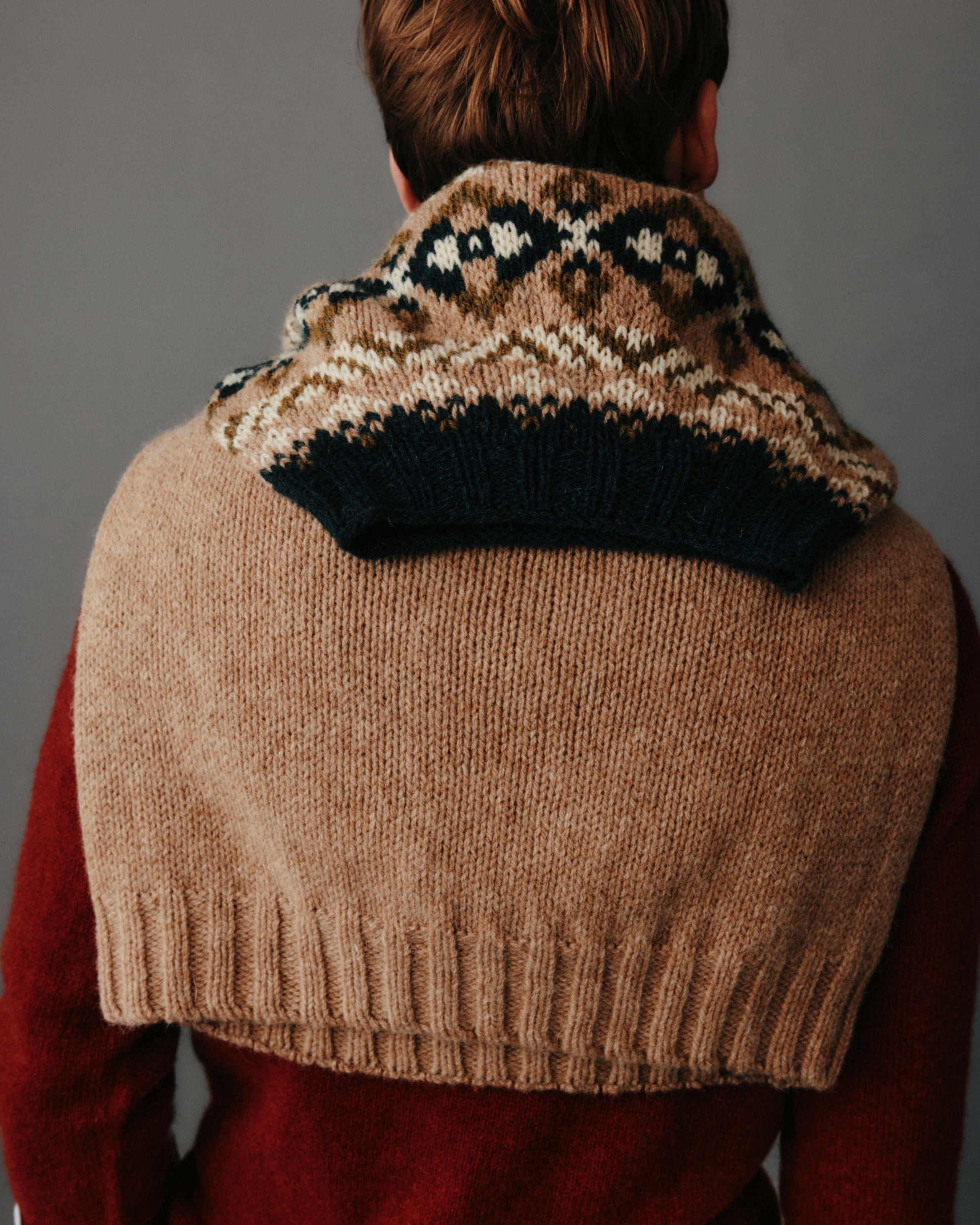 Person wearing a brown knitted vest with a patterned collar against a gray background