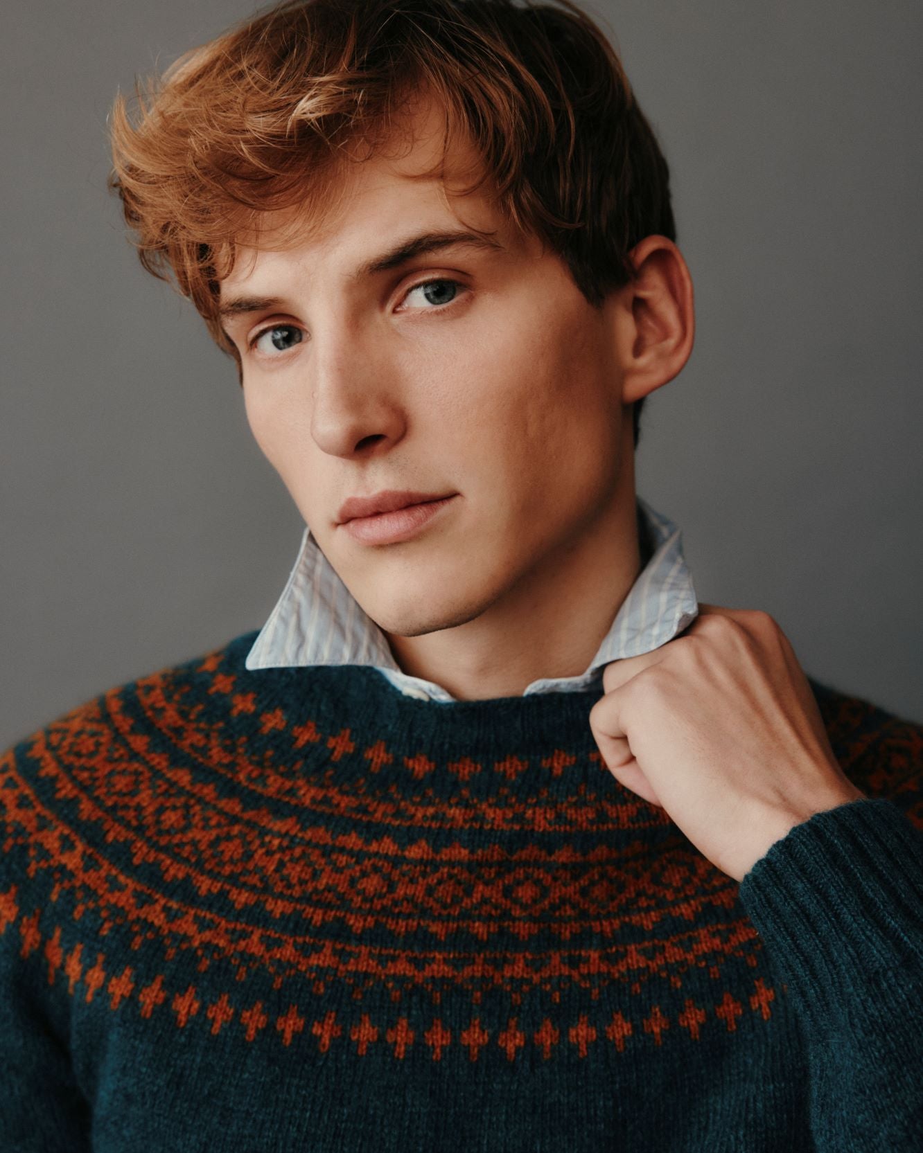 Man wearing a dark green sweater with red patterns against a gray background