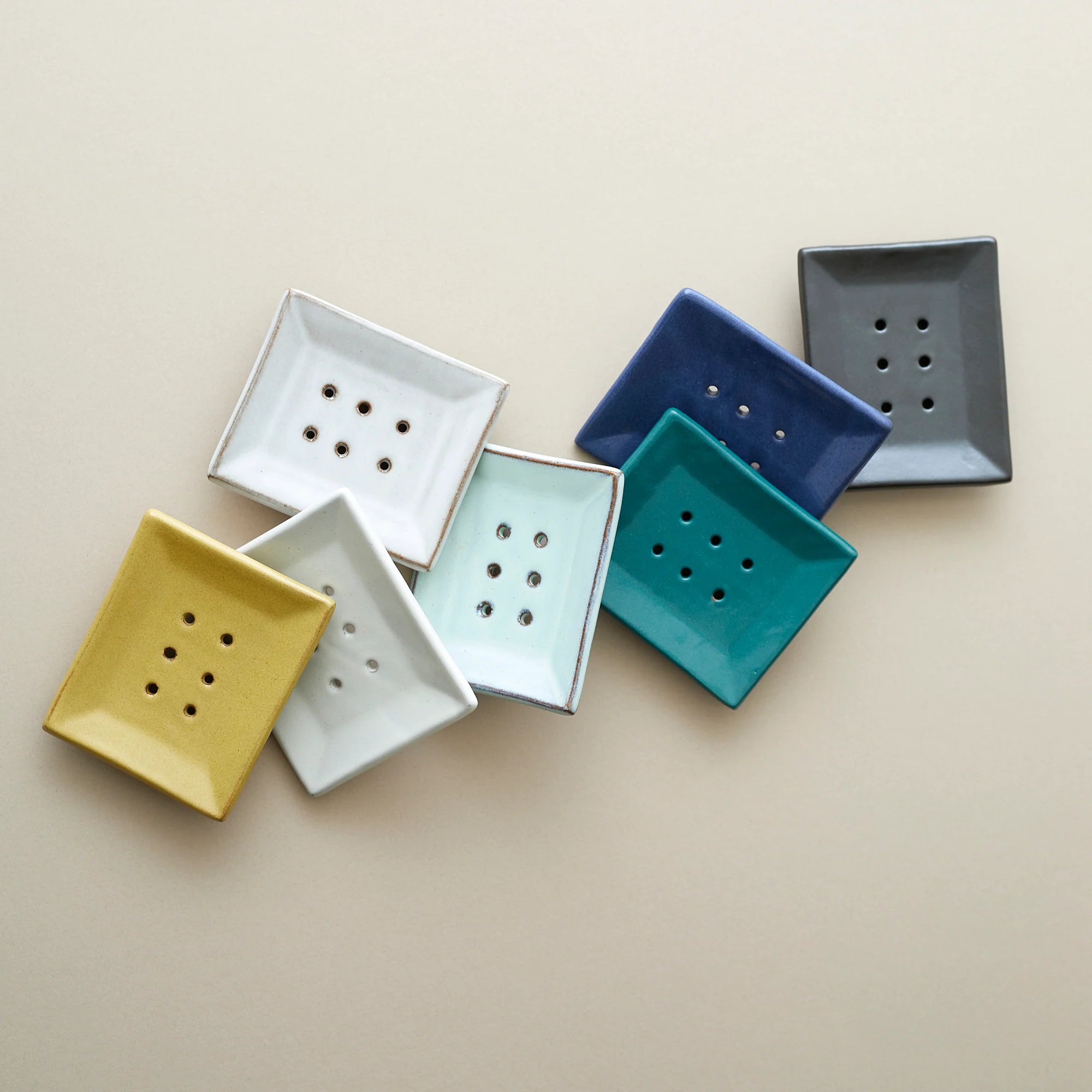 Collection of square ceramic soap dishes in various pastel colors, each with drainage holes.