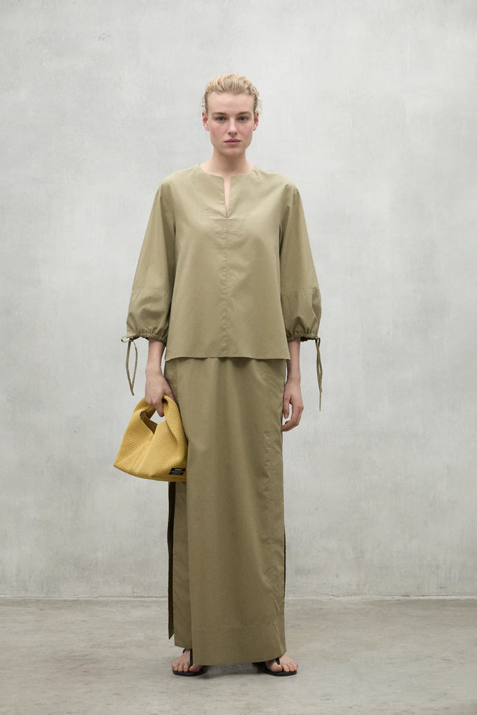 Model in a khaki Ecoalf outfit with balloon sleeves, paired with a yellow handbag, standing against a gray background.