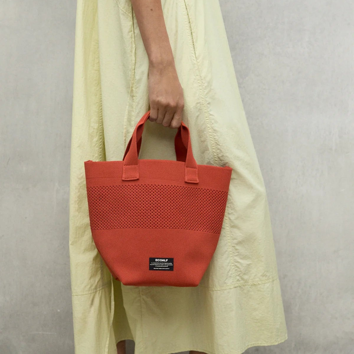 Terracotta-colored knit tote bag with short handles.  The bag has a small, rectangular brand label.
