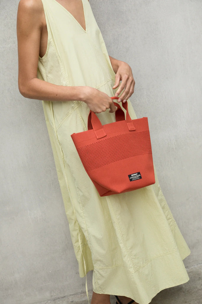A model in a pale yellow Ecoalf dress holds a bright red tote bag, showcasing sustainable fashion.