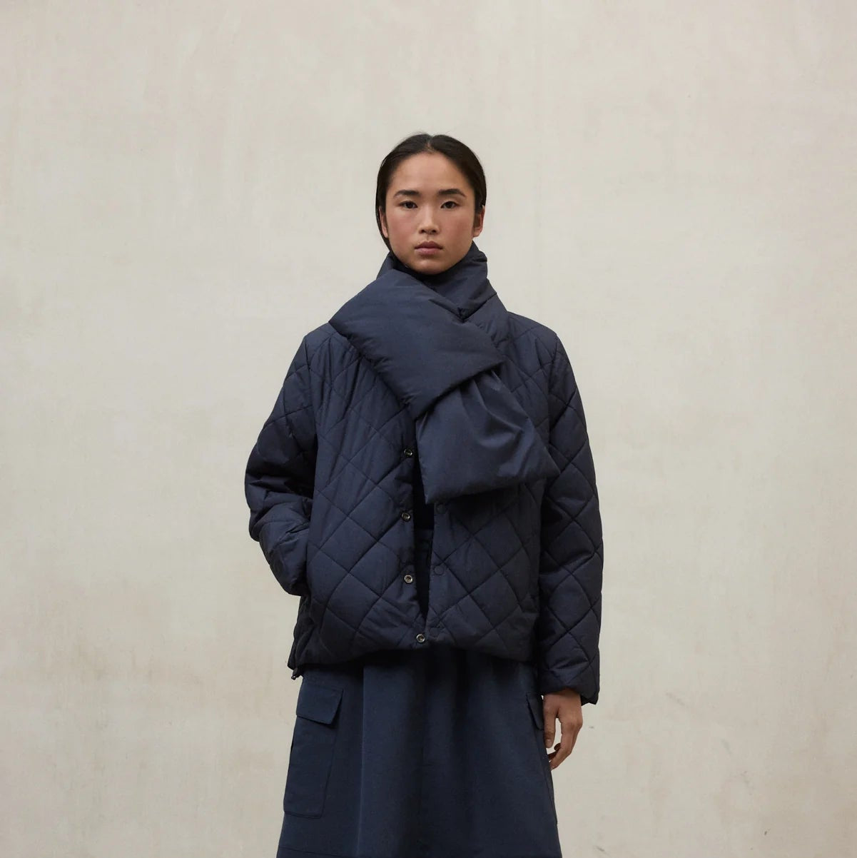 Person wearing a dark blue quilted jacket and long skirt against a plain background