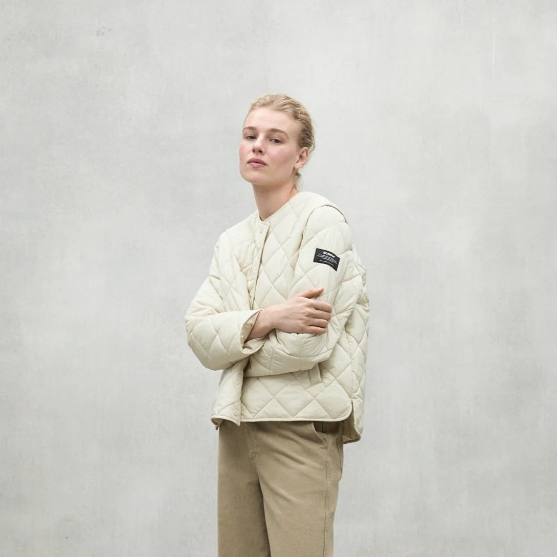 Cream-colored quilted jacket with a buttoned front and a small black label on the sleeve.