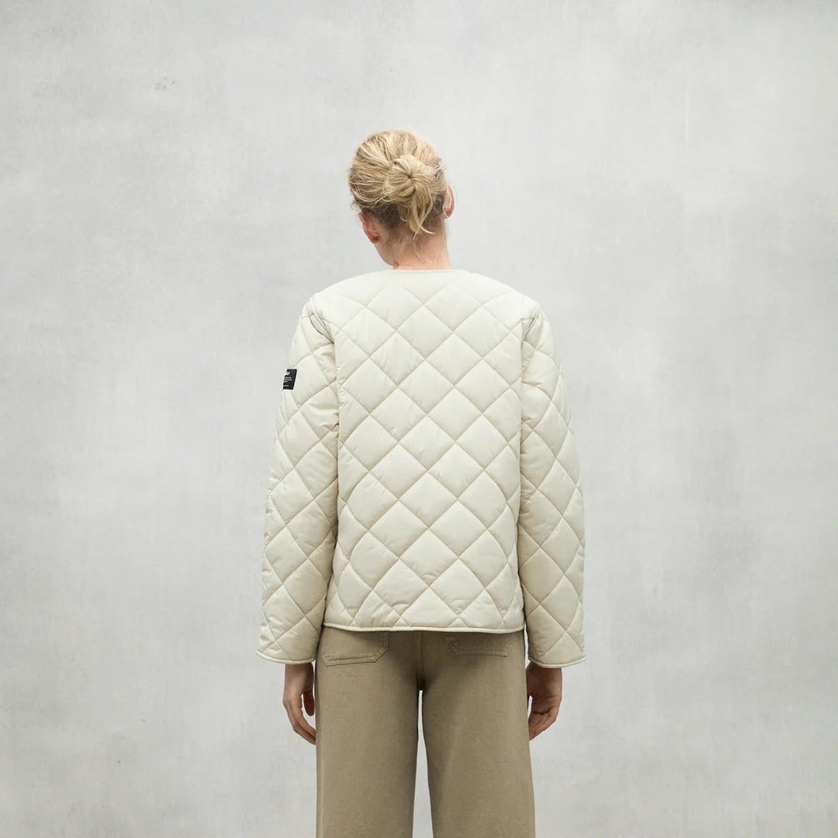 Cream-colored quilted jacket with diamond pattern stitching, seen from the back.