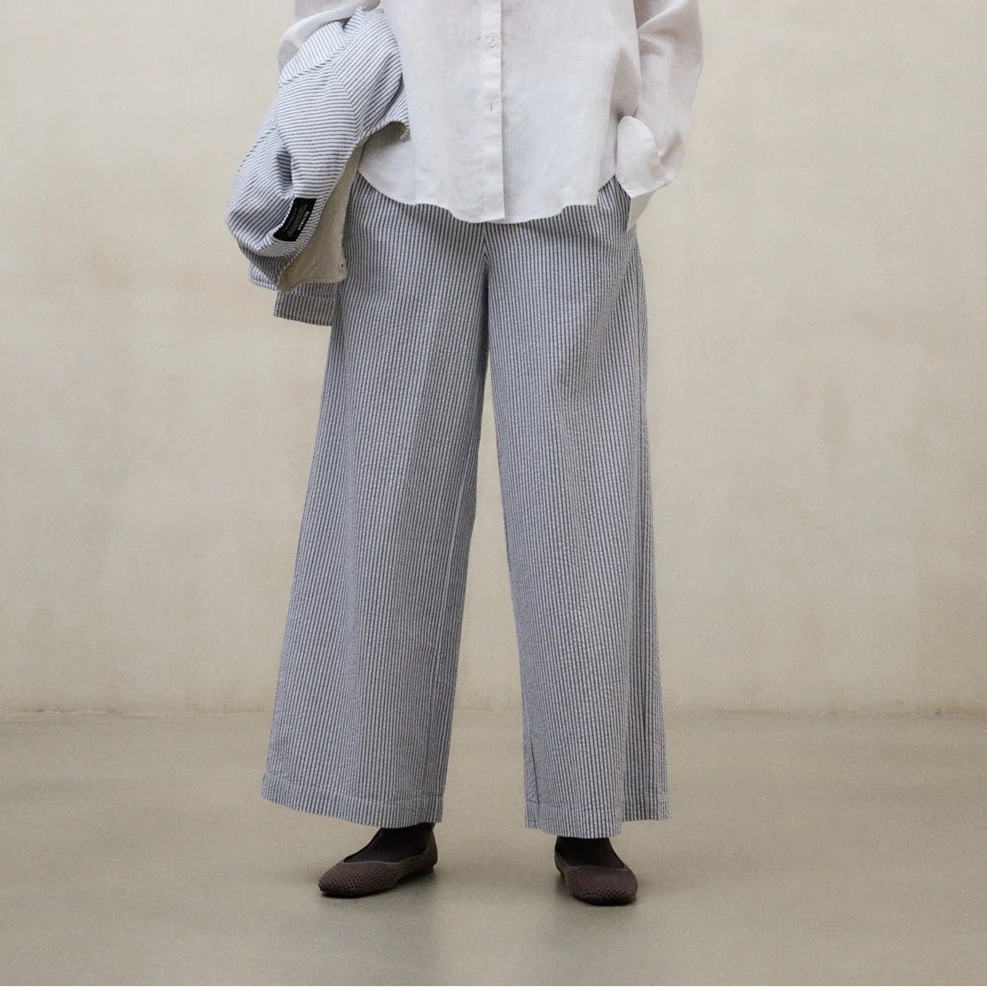 Person wearing a white shirt and blue and white pinstripe pants against a plain background