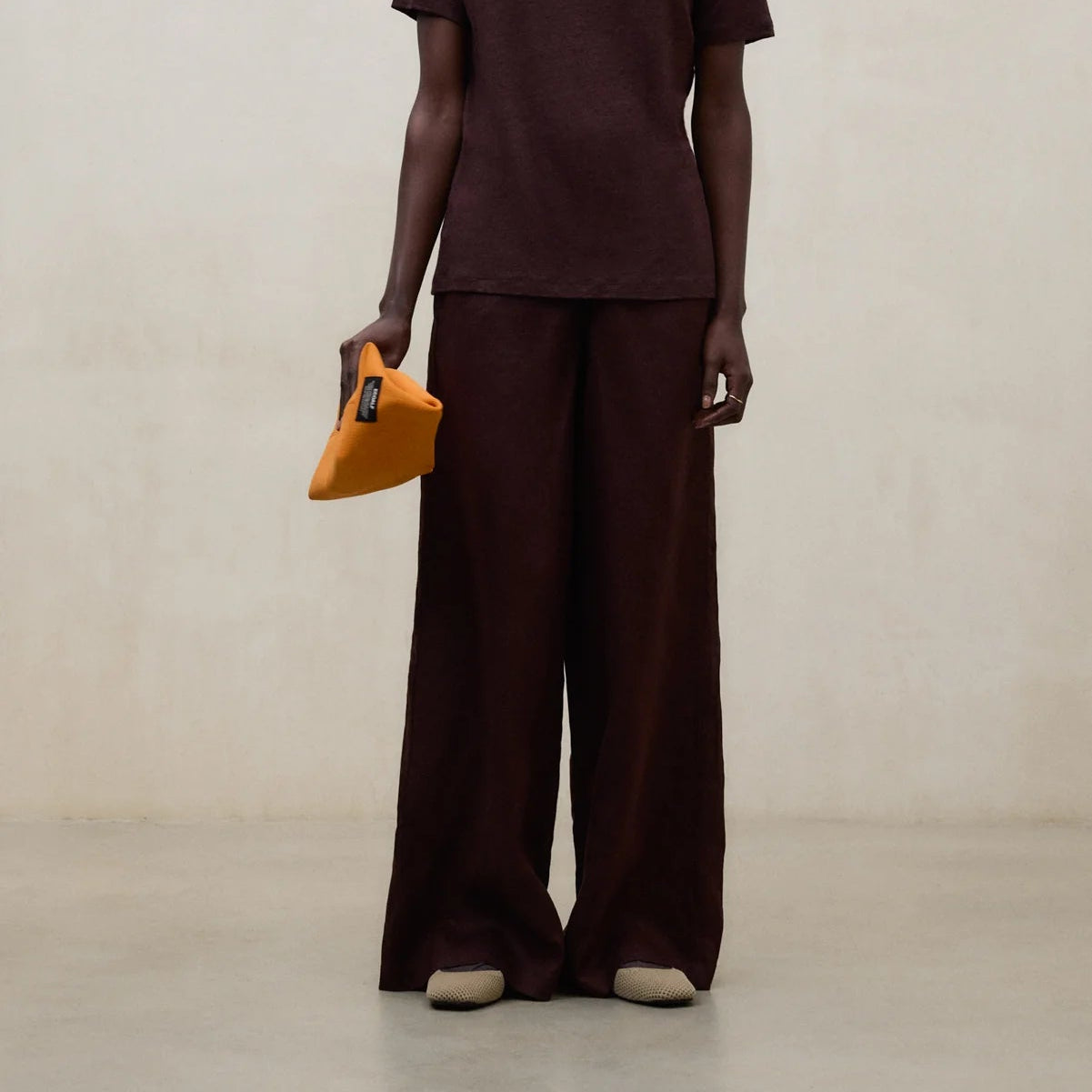 Person wearing a brown outfit holding a yellow bag against a plain background