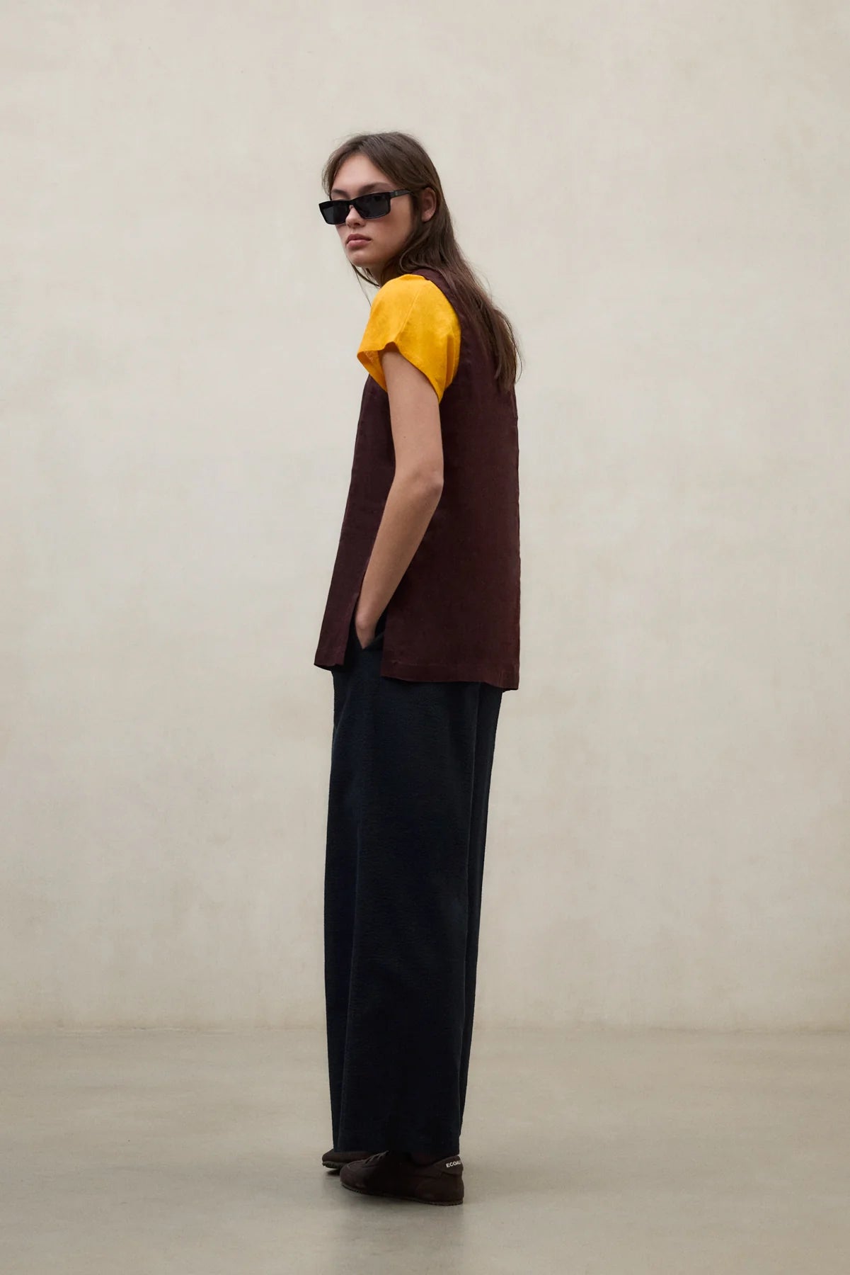 Person wearing a brown sleeveless top and black pants against a plain background