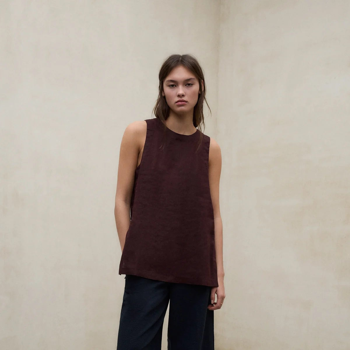 Person wearing a sleeveless brown top and wide-leg black pants against a plain background