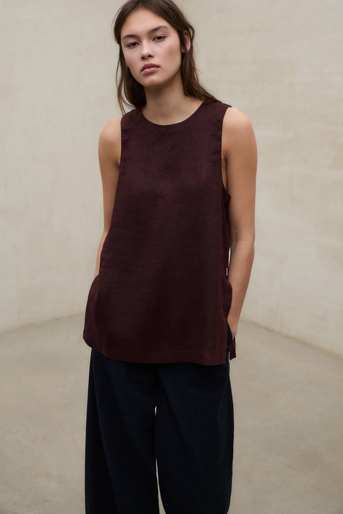 Woman wearing a brown sleeveless top and black pants against a beige background