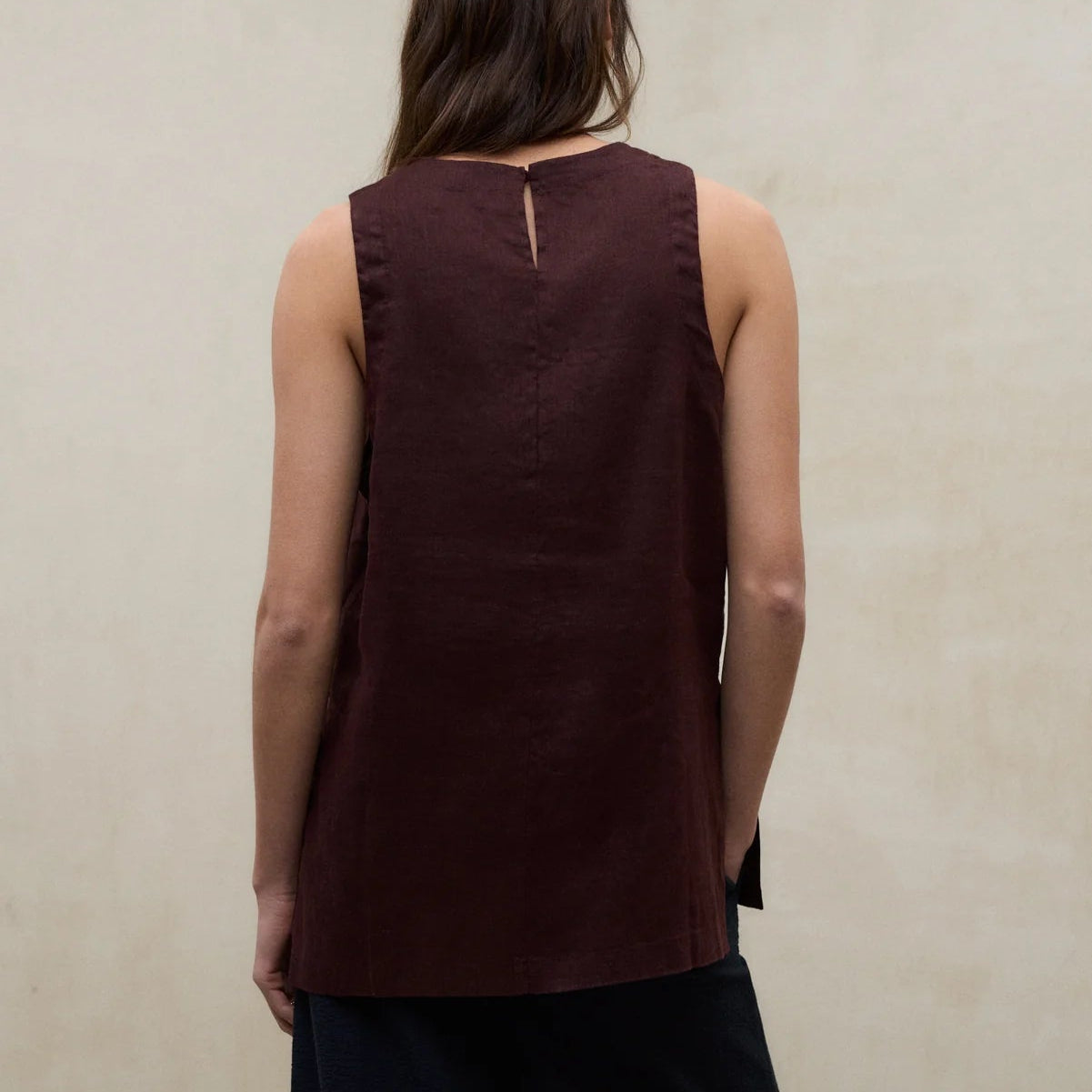 Woman wearing a brown sleeveless top and black pants against a plain wall.