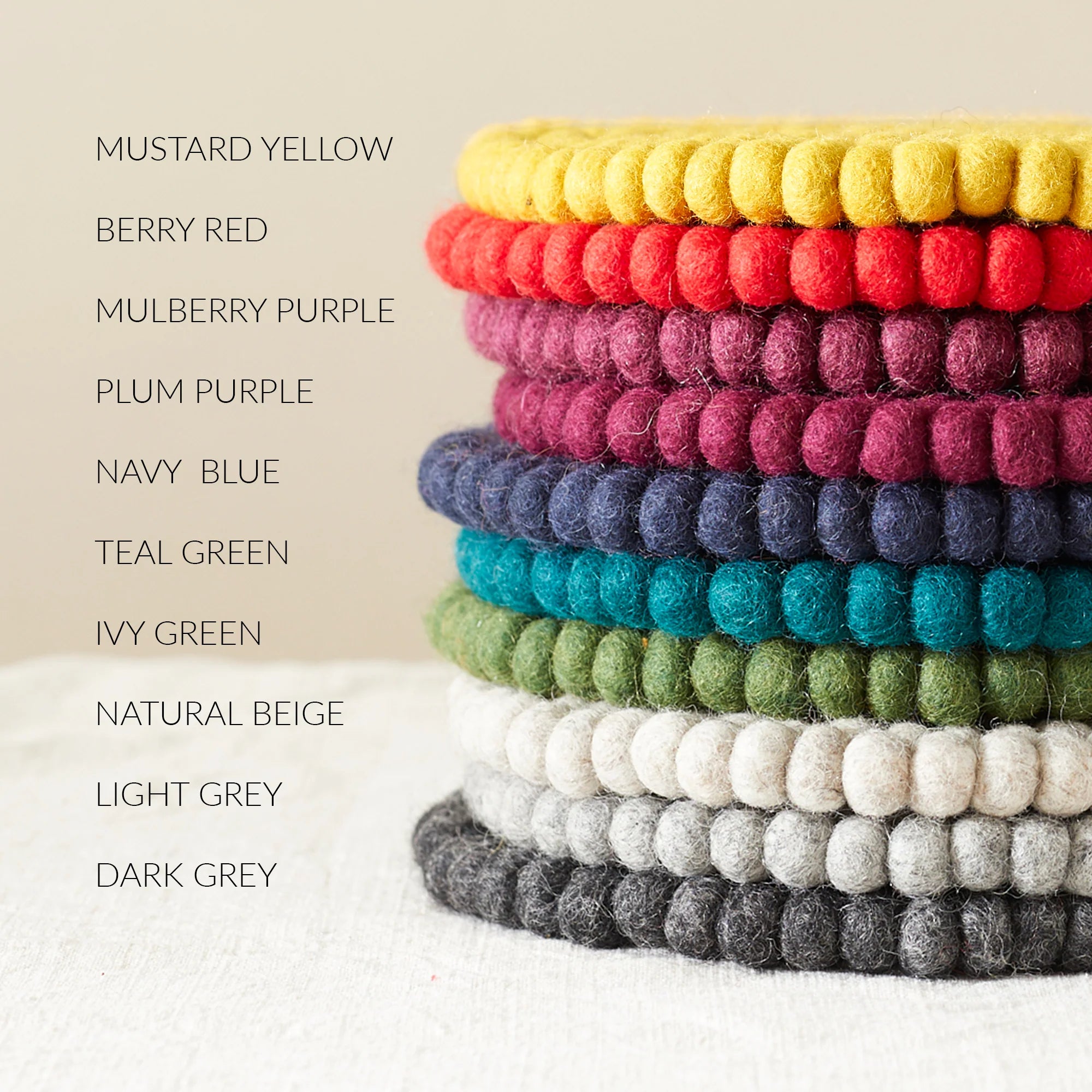 Stack of round felt coasters in various colors: mustard yellow, berry red, mulberry purple, plum purple, navy blue, teal