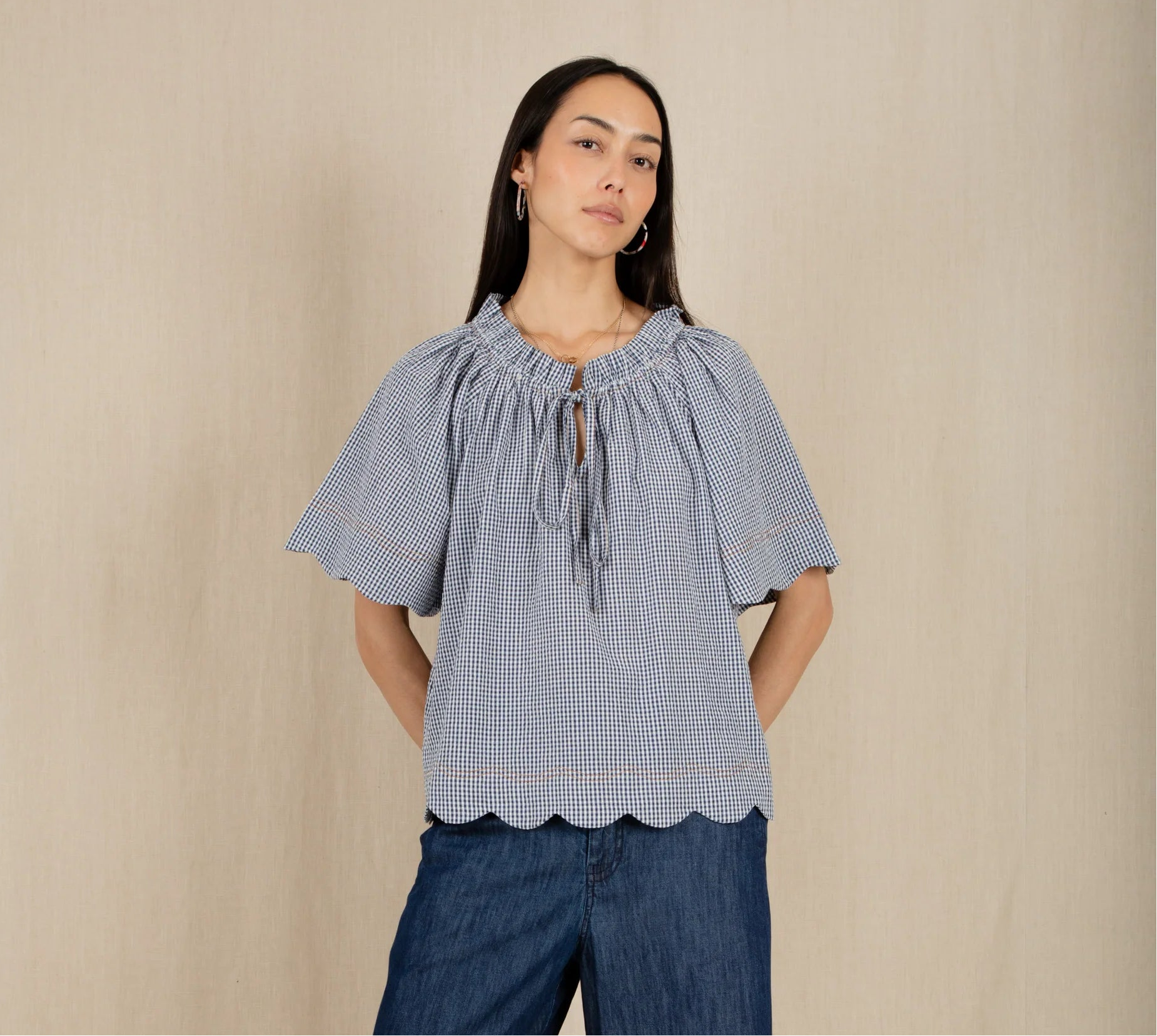 Woman wearing a blue top and dark blue pants standing against a beige wall with a white floor.