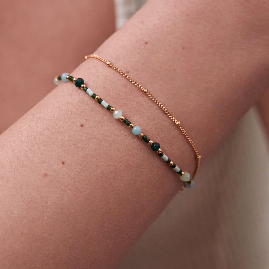 Beaded bracelet with light blue and dark green stones, and a gold chain bracelet layered on top.