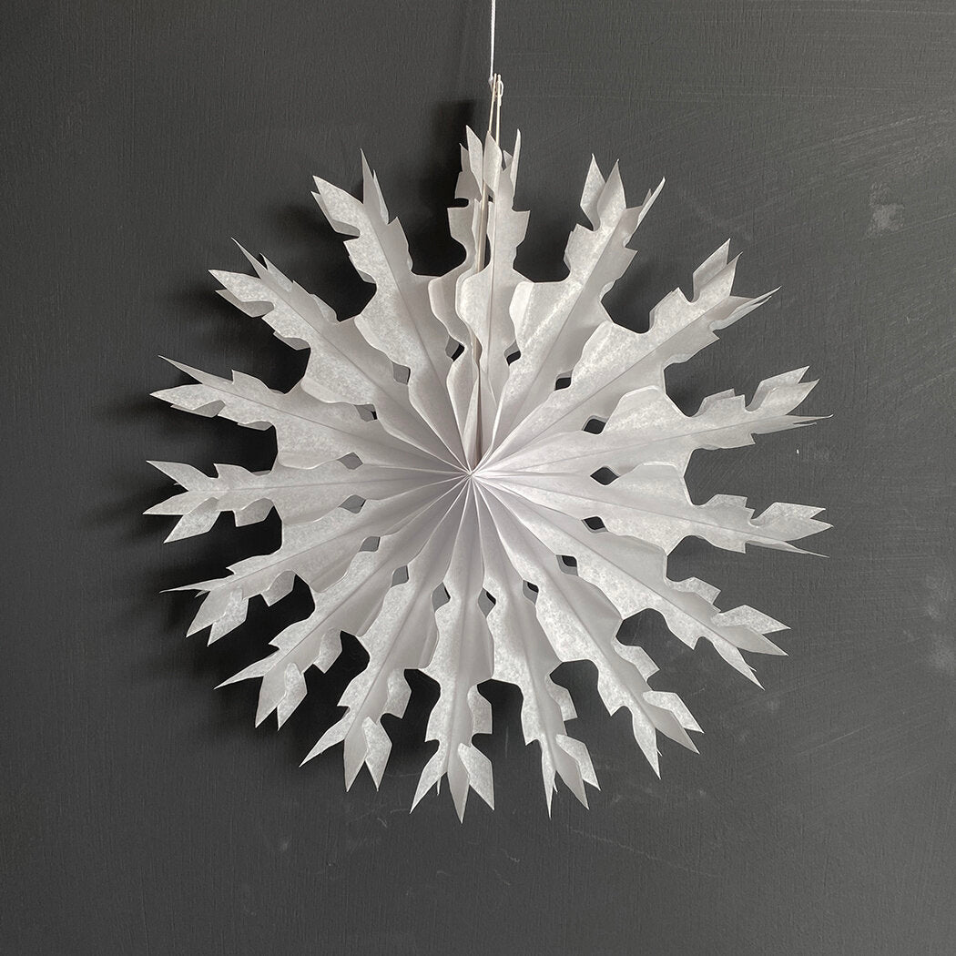 Large white paper snowflake decoration with a folded, layered design and pointed edges, hanging against a dark gray