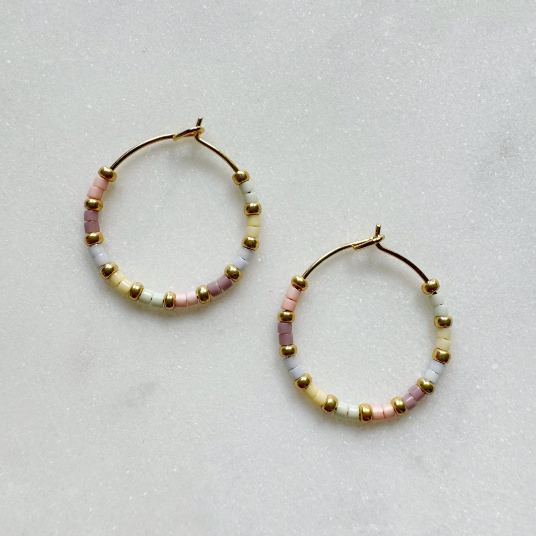 Gold hoop earrings adorned with pastel pink, lavender, and cream-colored beads.