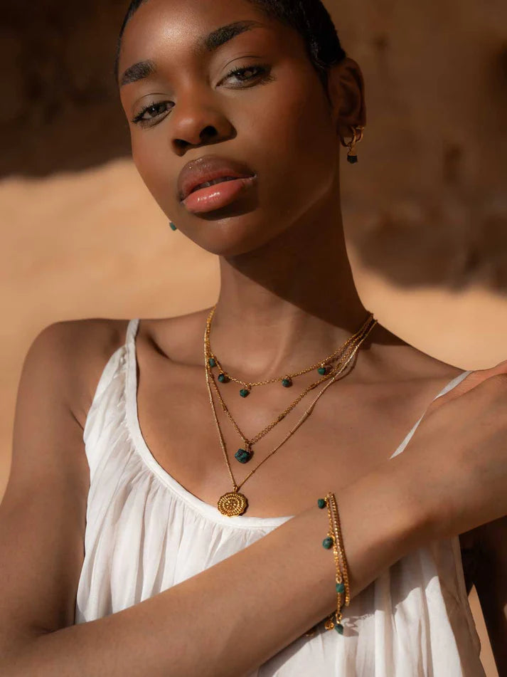 Woman wearing gold necklaces and bracelets against a warm-toned background