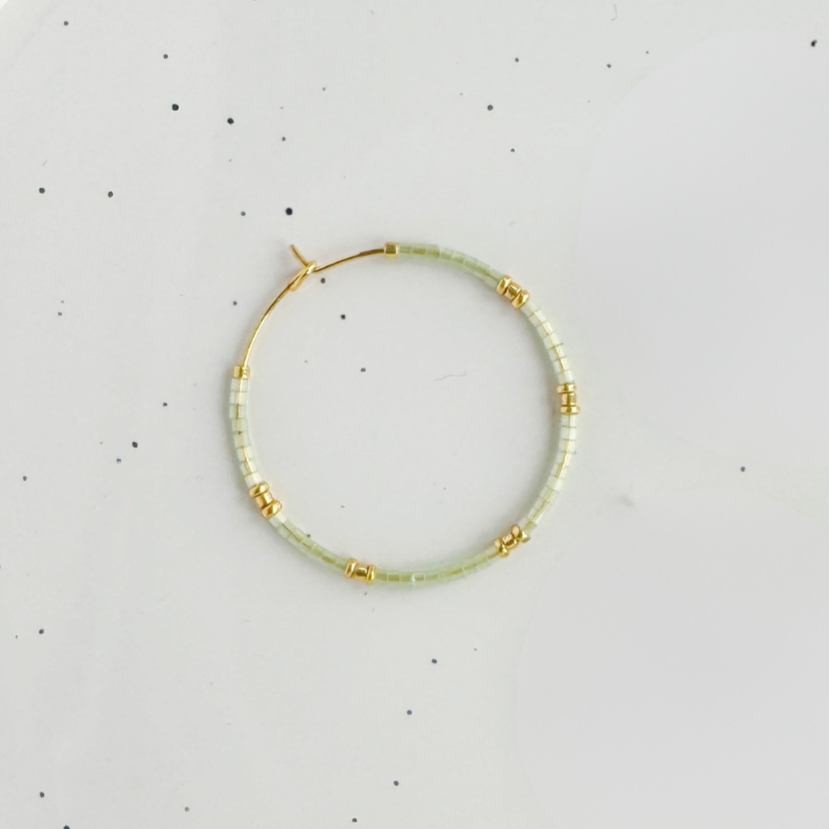 Gold hoop earring with pale green seed beads.