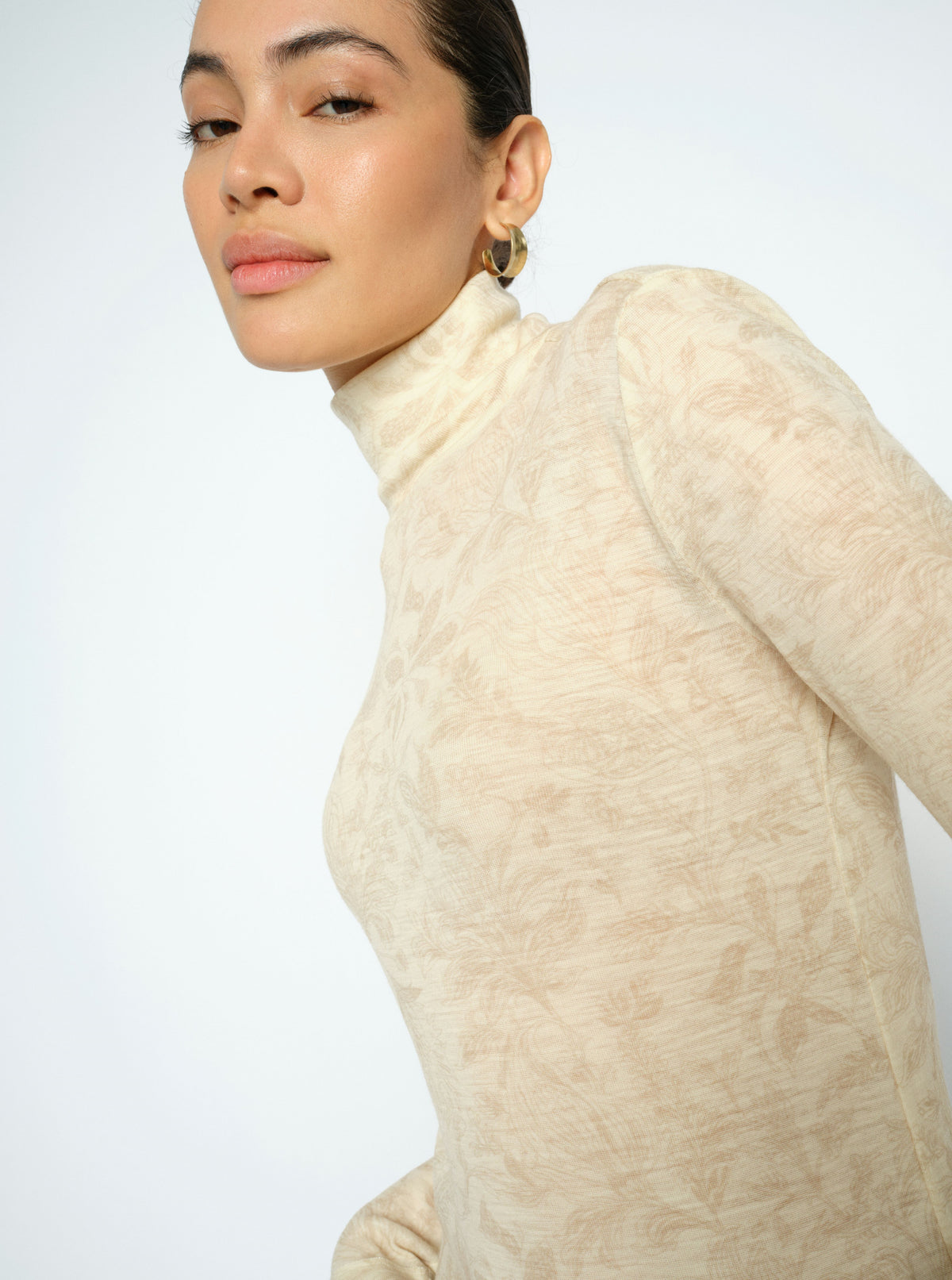 Woman wearing a beige turtleneck sweater against a white background