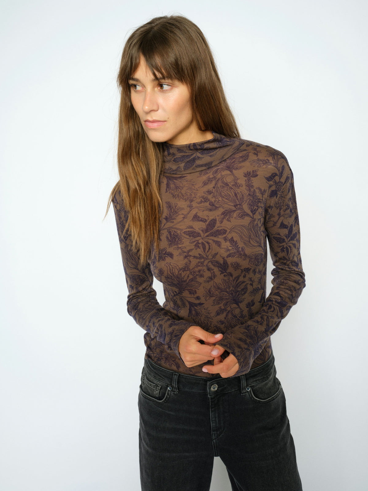 Woman wearing a patterned long-sleeve top and black jeans on a white background