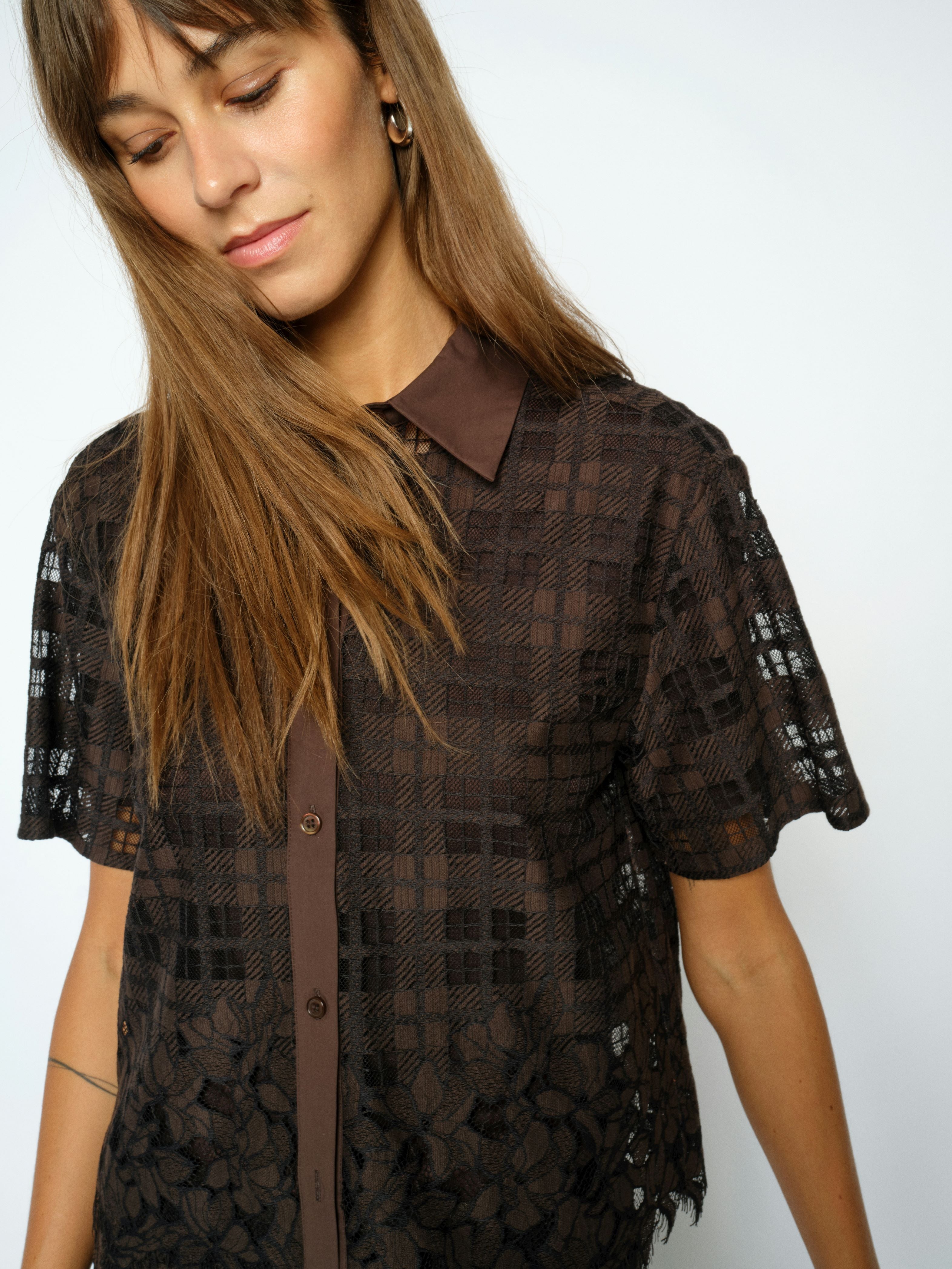 Woman wearing a dark lace blouse with a plain background