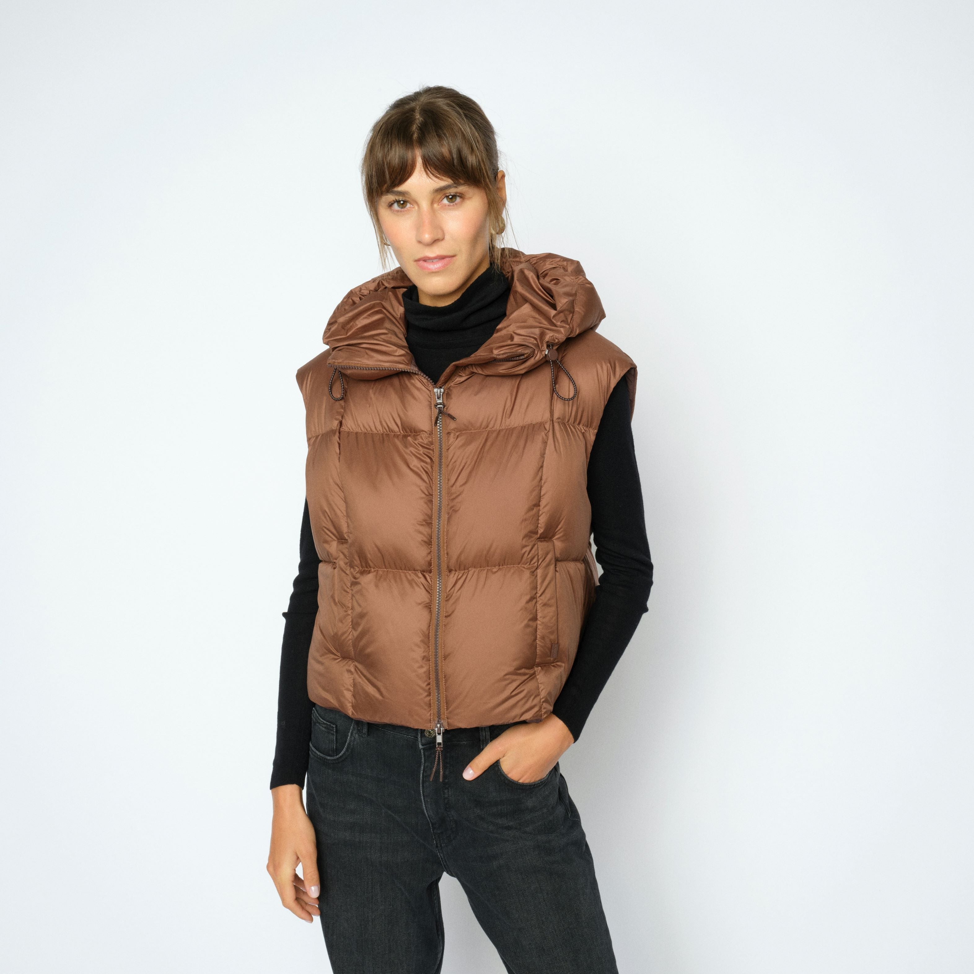 Person wearing a brown puffer vest on a white background