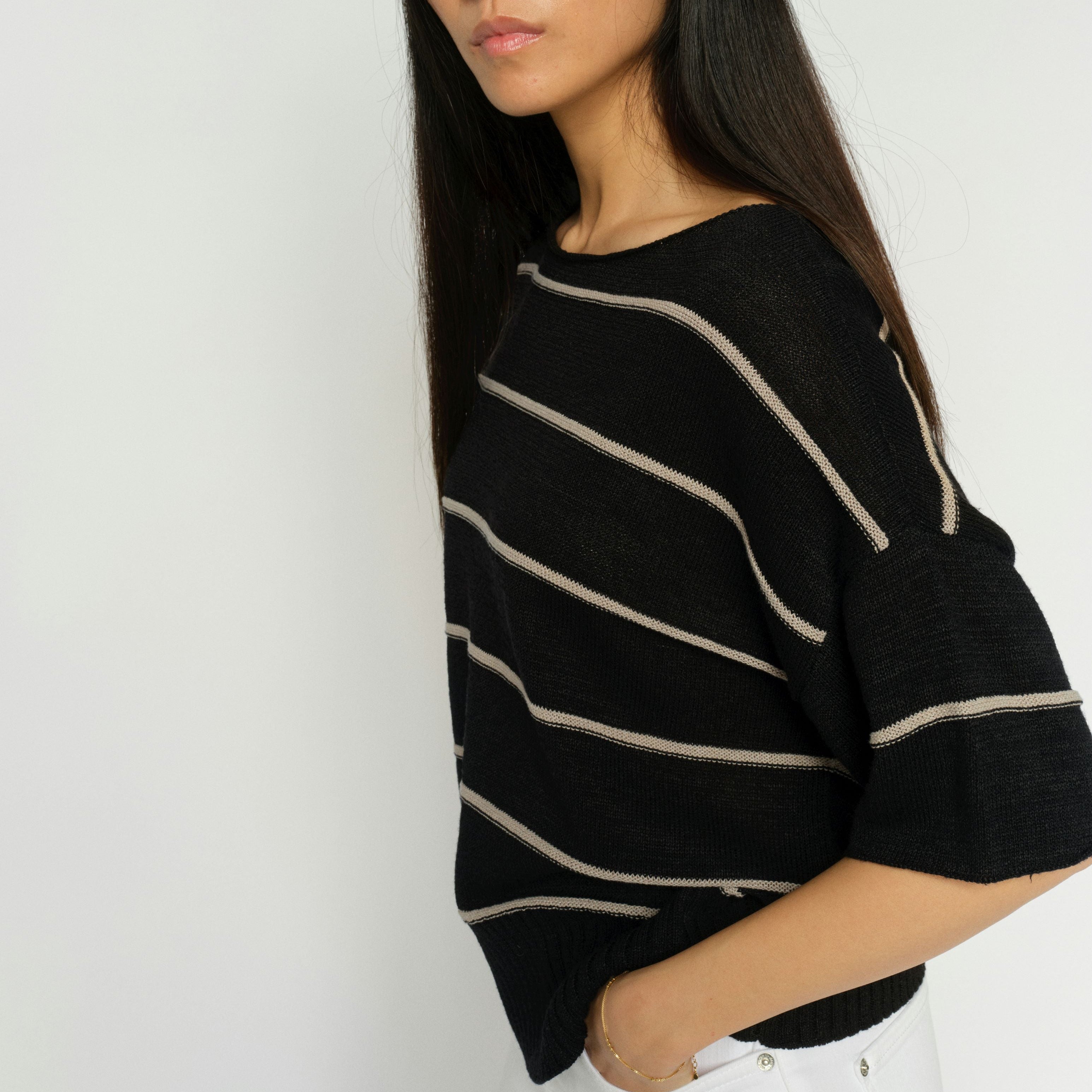 Woman wearing a black sweater with white stripes against a plain background