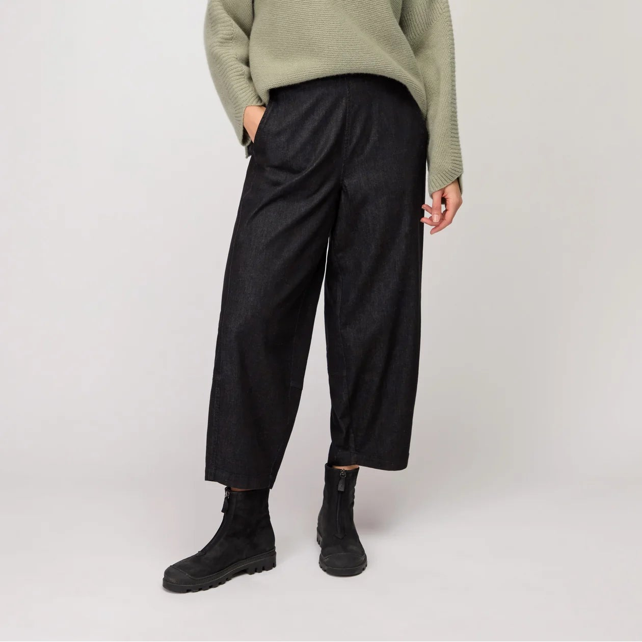 Woman wearing a green sweater, black pants, and a yellow scarf on a white background
