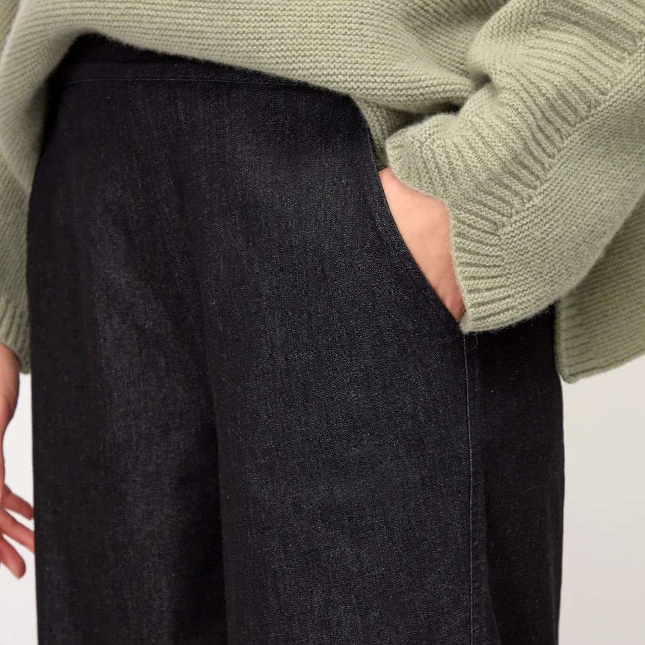 Person wearing a green sweater and dark pants against a white background