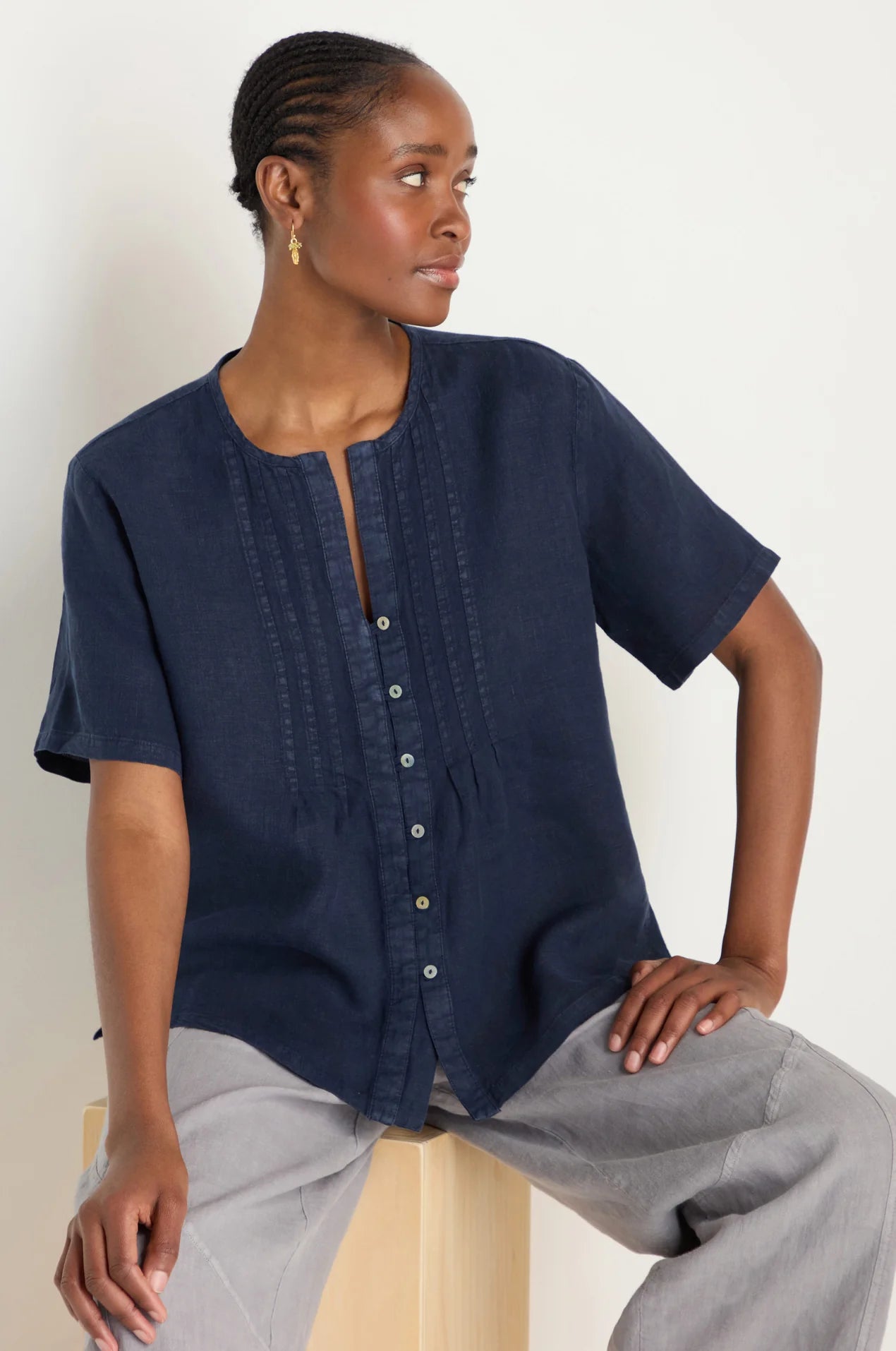 Woman wearing a navy blue top with short sleeves and light gray pants against a white background