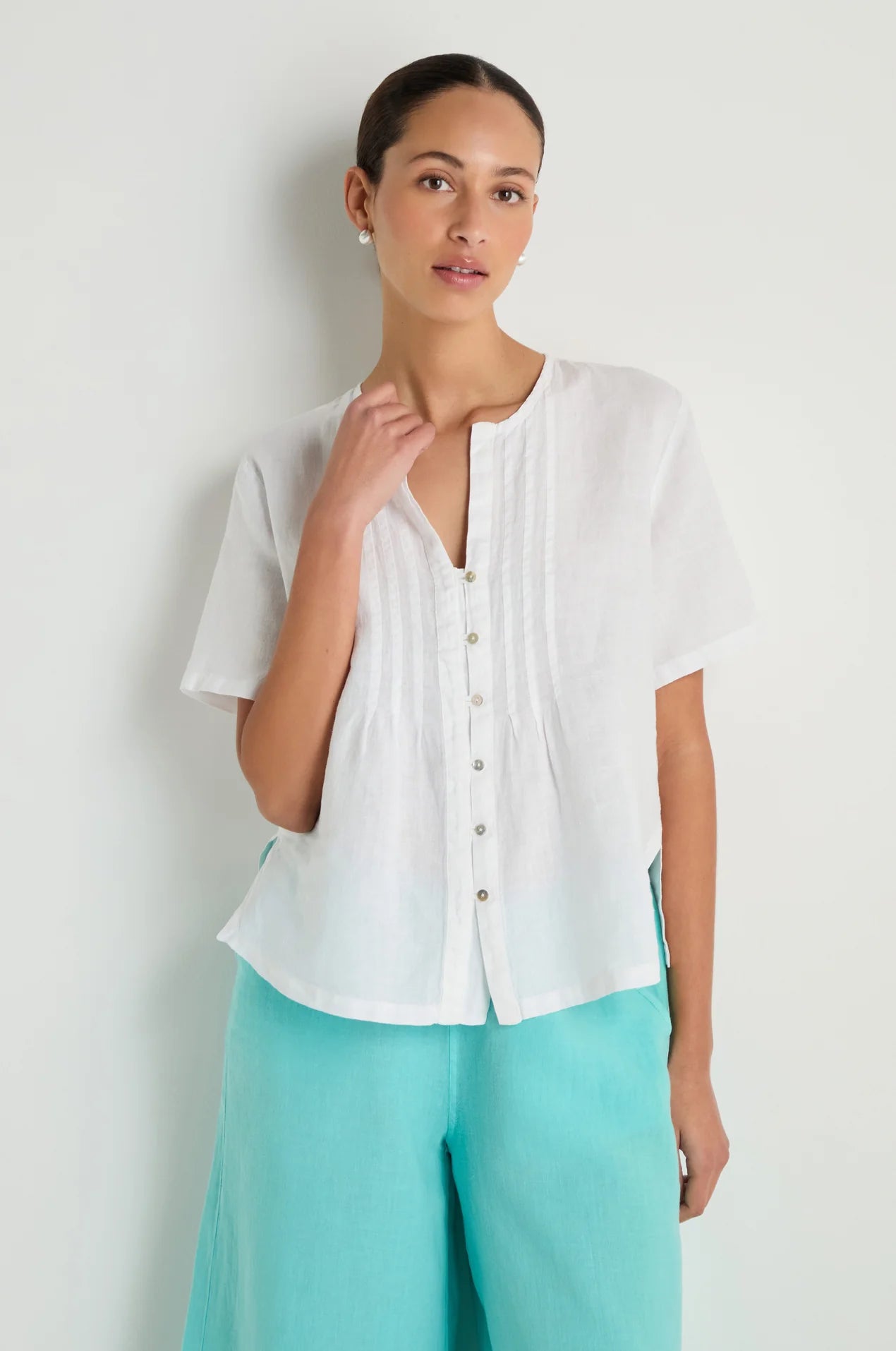 Woman wearing a white blouse and turquoise pants against a light gray background