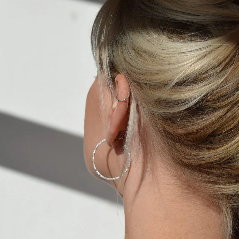 Silver hammered hoop earrings worn in a woman's ear.