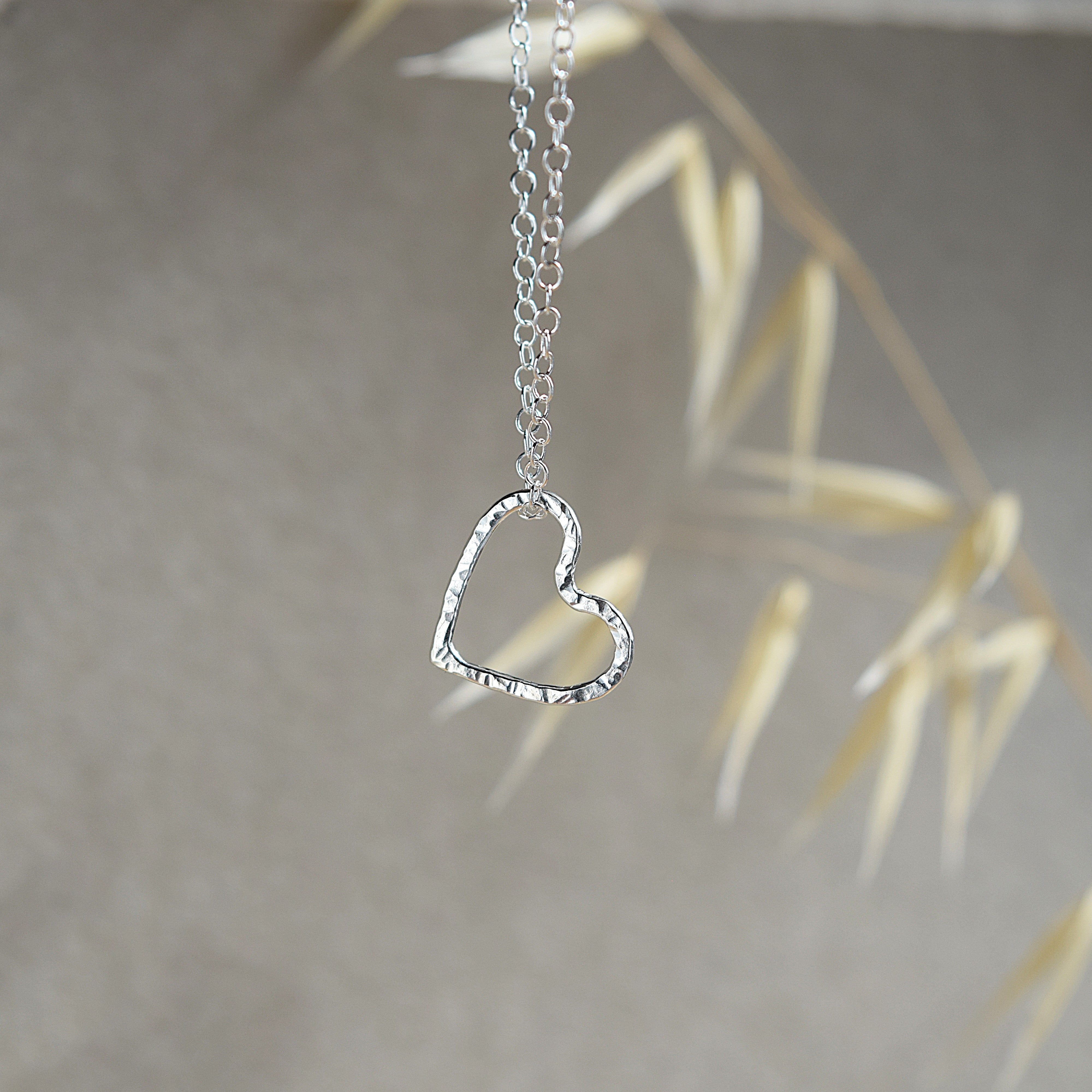 Silver heart-shaped pendant on a chain against a neutral background